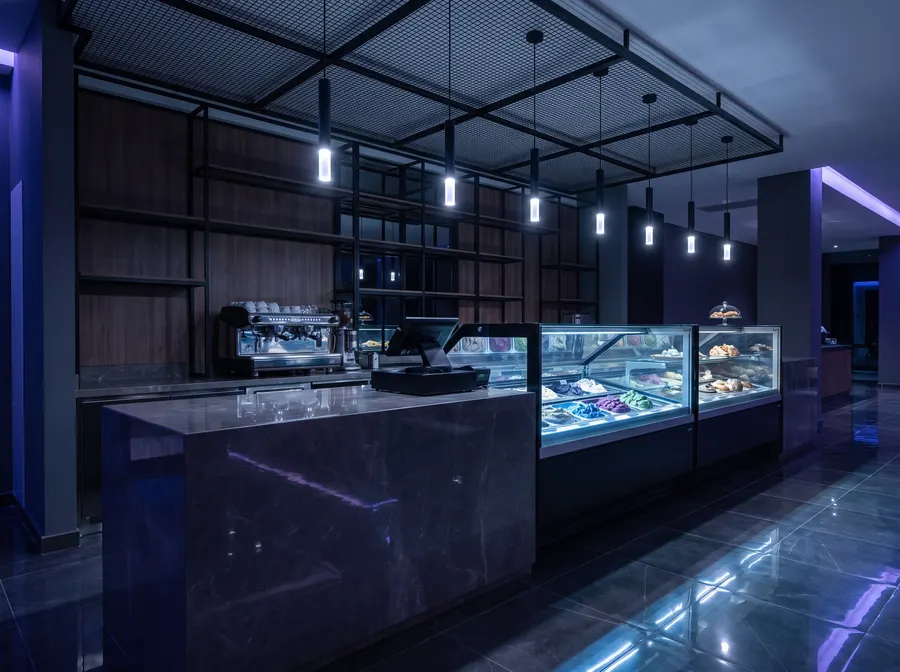 Generated scene: an empty café counter at night with an espresso machine and a lit gelato case, in blue and violet light.